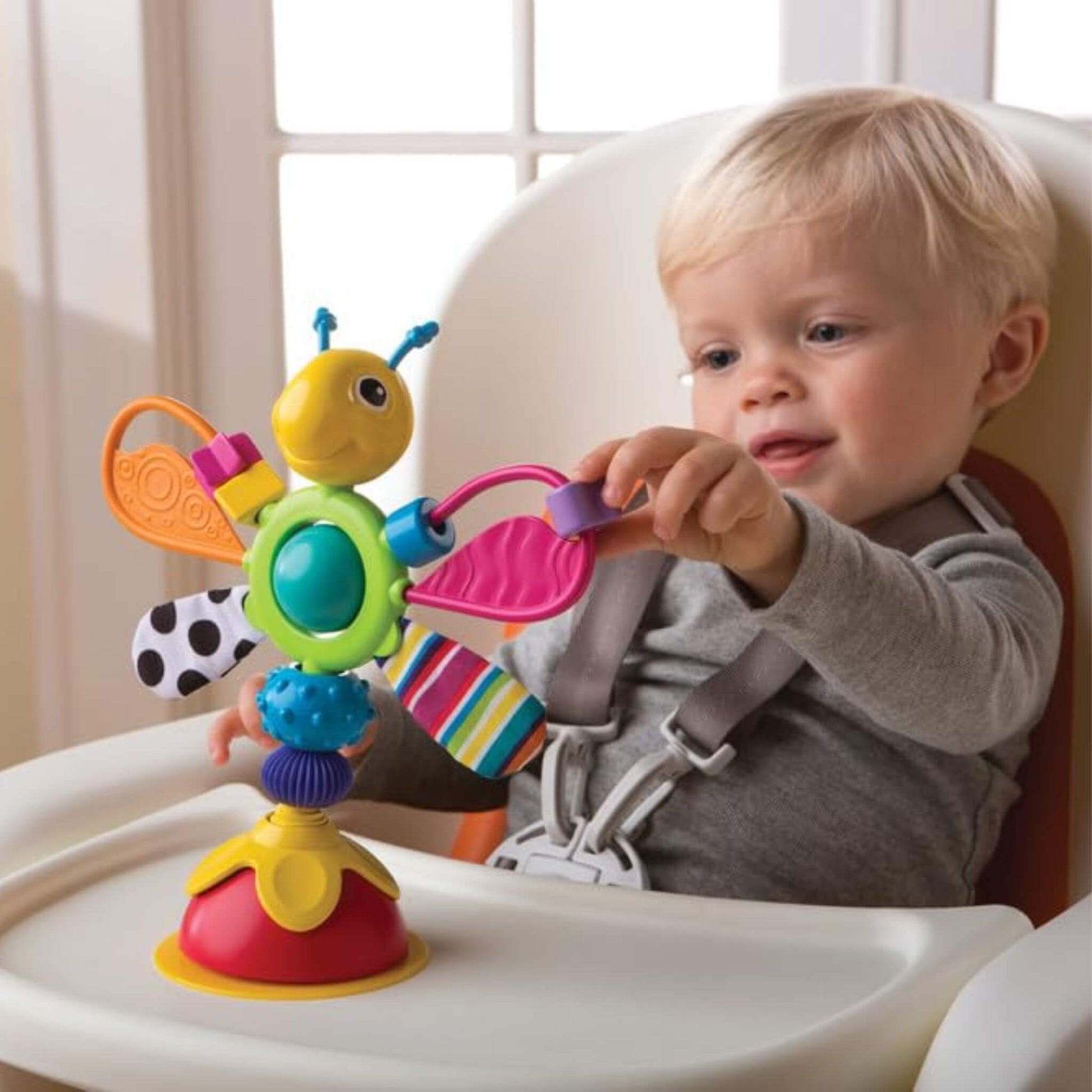 Toddler exploring a suction-based activity toy with bright colours and textured surfaces during mealtime play.