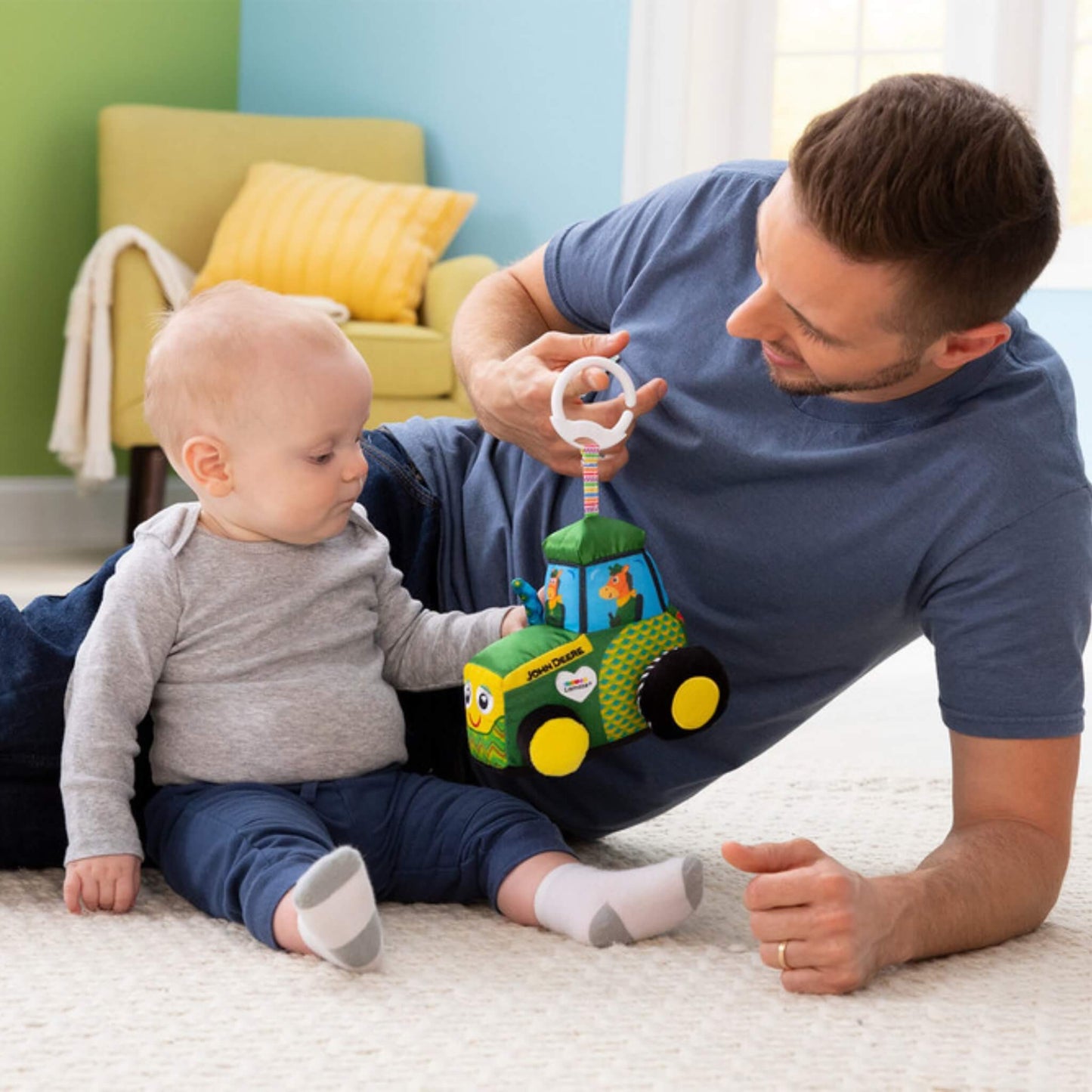 Baby sitting with an adult on the floor, exploring the soft tractor toy during playtime.