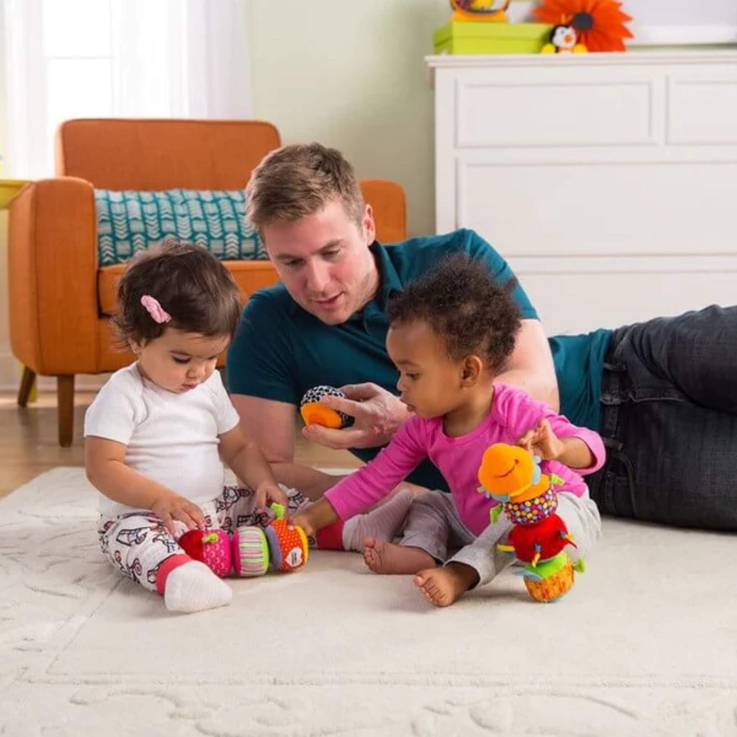 Two toddlers sitting on a rug with a father nearby, each playing with colourful caterpillar toys featuring detachable segments.