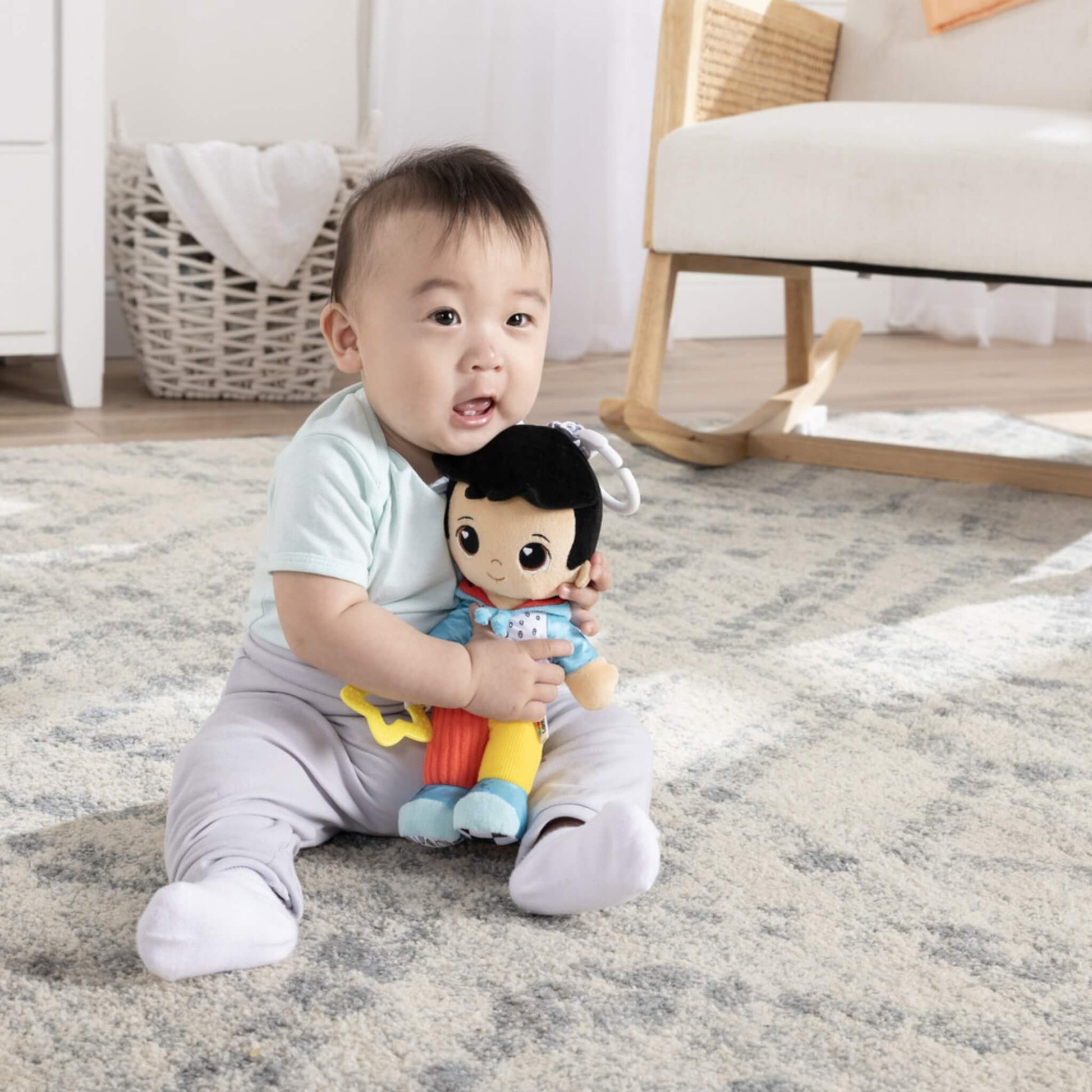 Baby sitting on the floor hugging a colourful doll dressed in blue, red and yellow, smiling and playing with its soft textures.