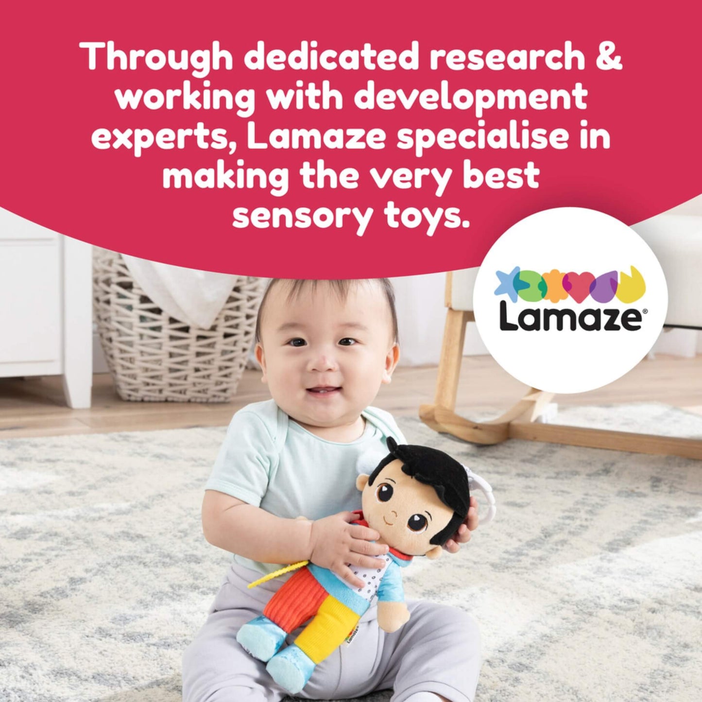 Baby sitting on the floor holding a colourful doll while smiling, with text about Lamaze toys being designed with development experts.