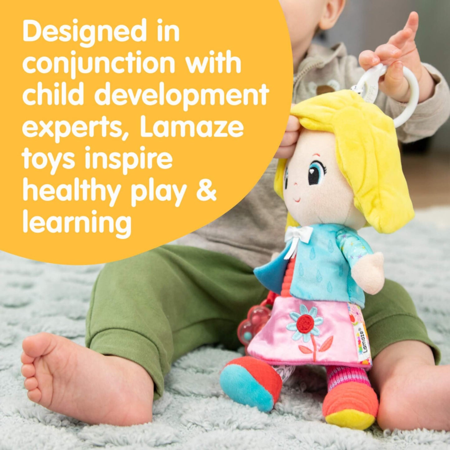 Baby sitting on a rug holding a bright doll while text highlights its developmental design encouraging learning and healthy play.