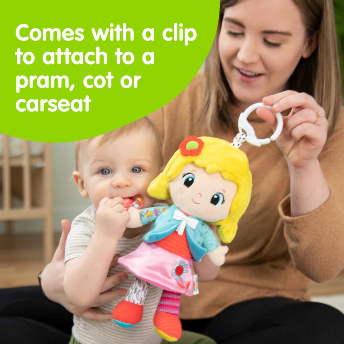 Parent holding a colourful soft doll with a white clip, showing how it can attach easily to a pram, cot or car seat for travel and play.