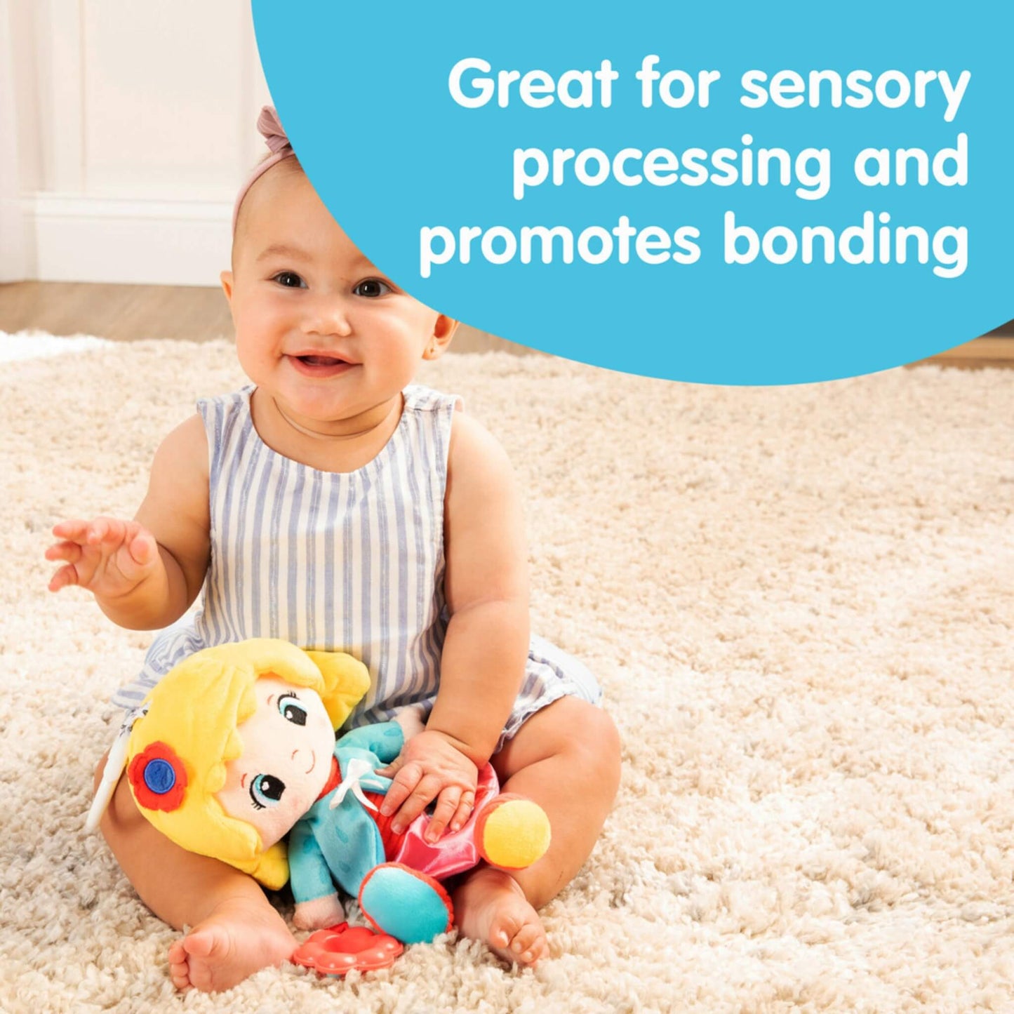 Baby sitting on a cream rug smiling with a soft doll in their lap while text describes how the toy supports sensory processing and bonding.
