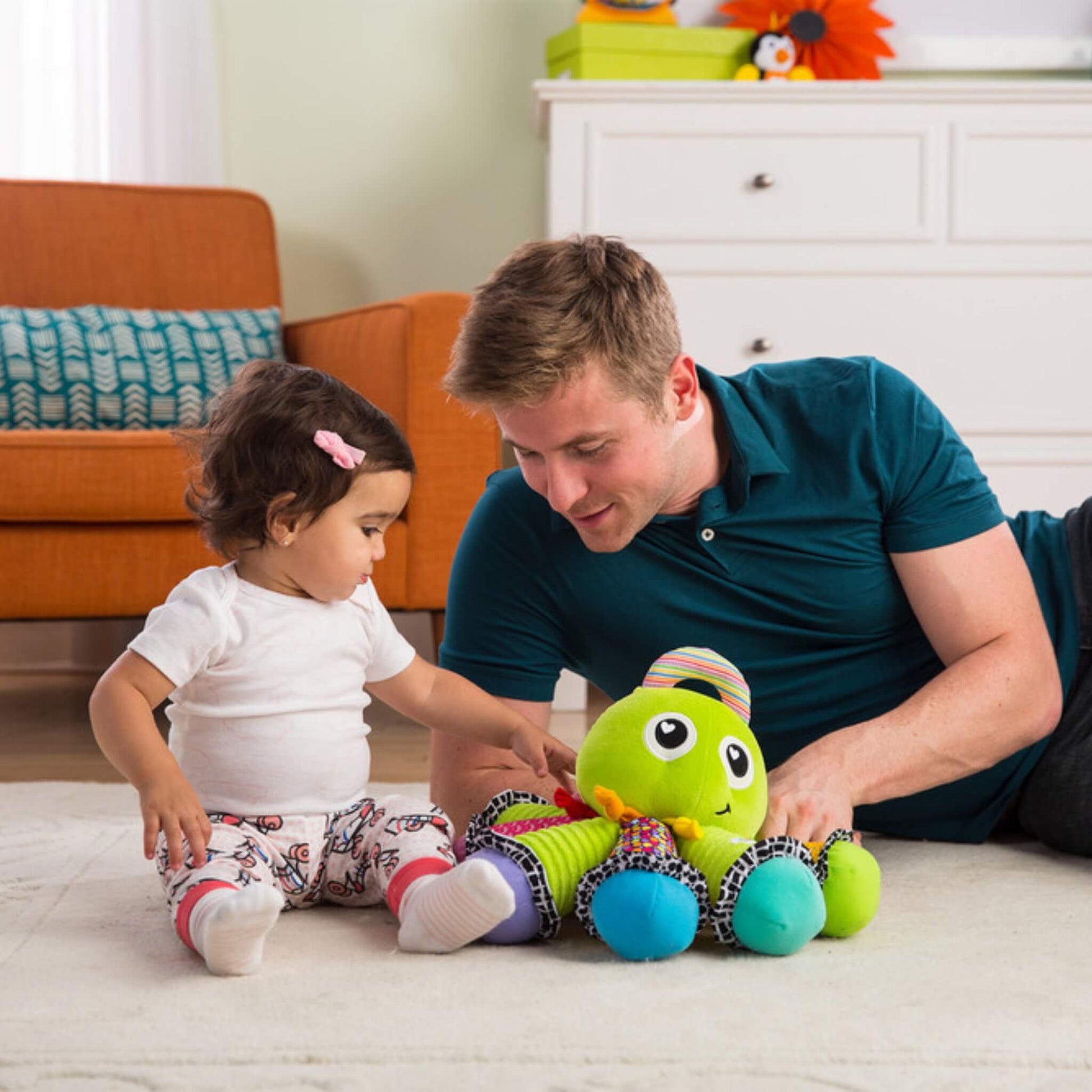Toddler and adult playing on a light rug, with the soft octopus toy between them as they press and touch its textured legs.