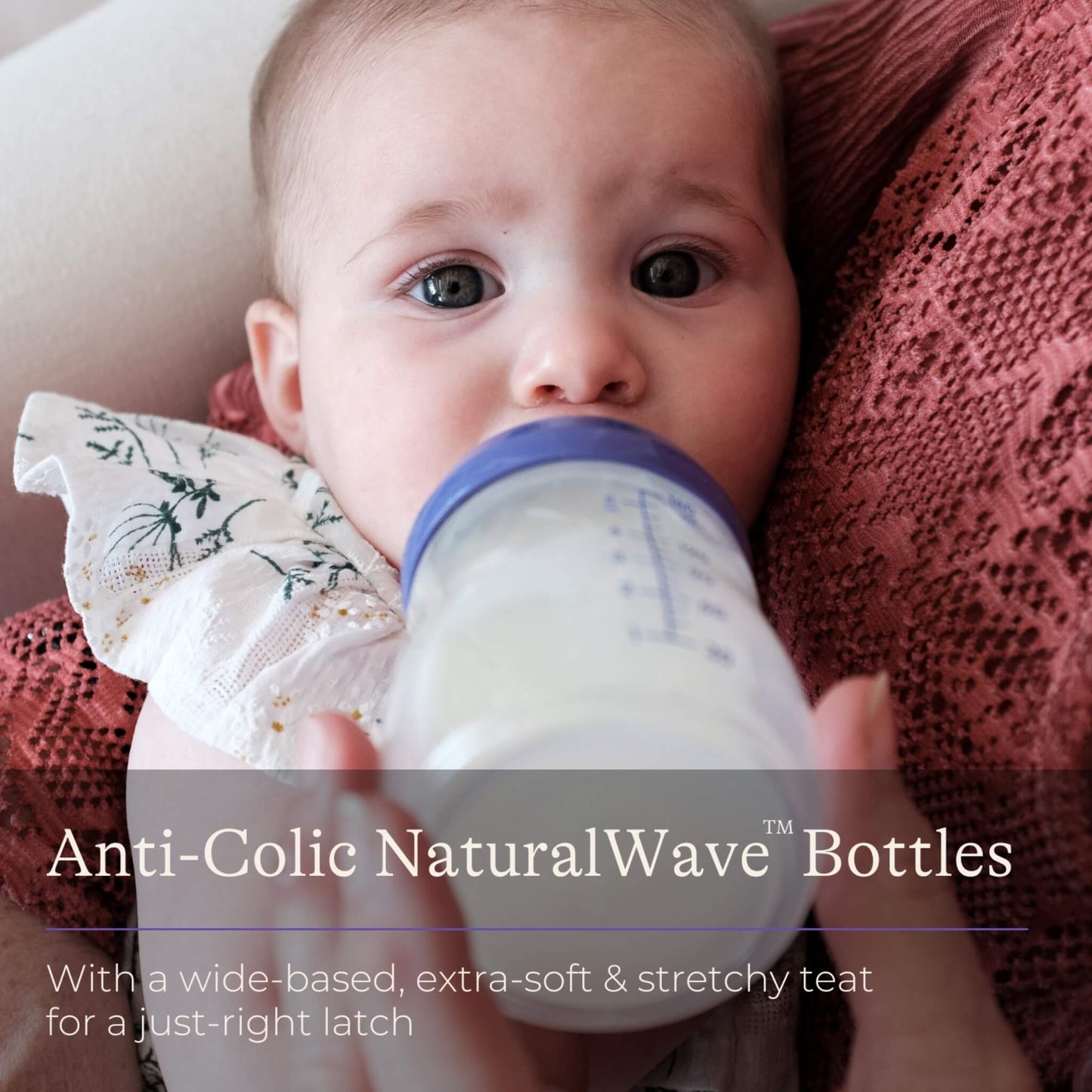Baby being bottle fed while resting against an adult, drinking from a wide-neck feeding bottle with milk visible inside.
