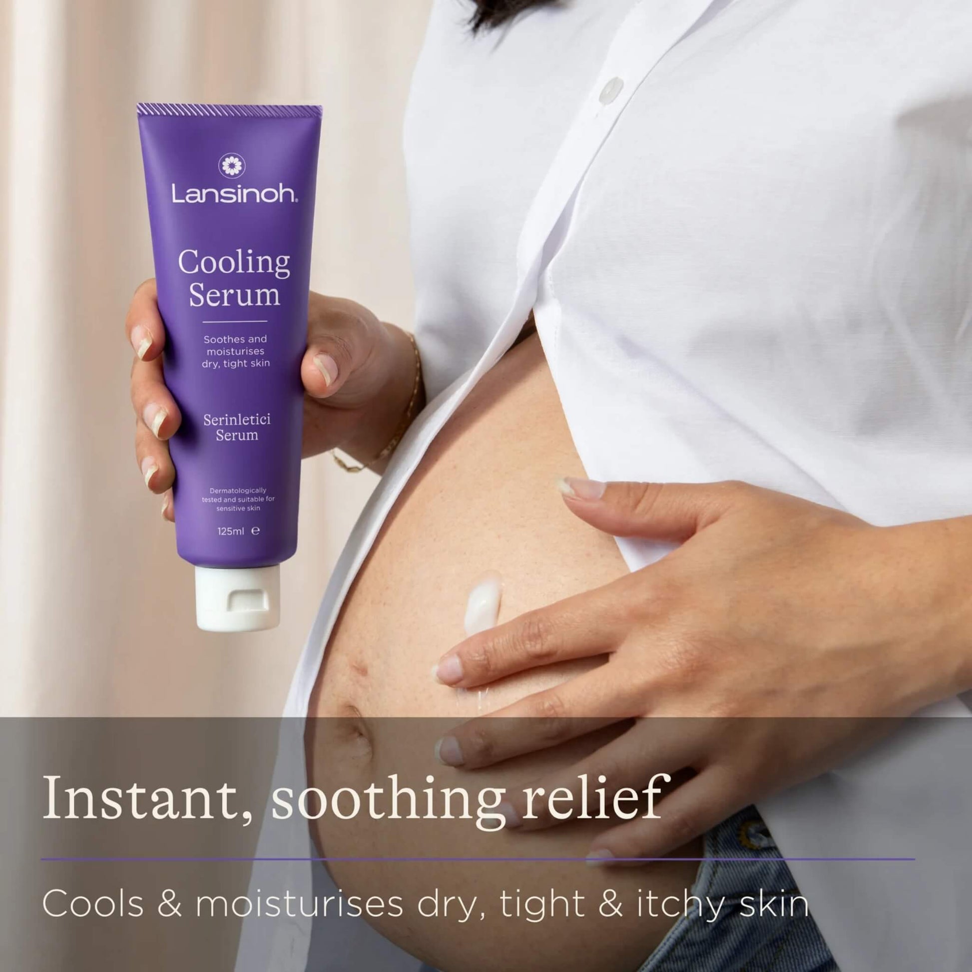 A pregnant woman applies cooling serum to her baby bump while holding a purple tube of skincare beside her abdomen.