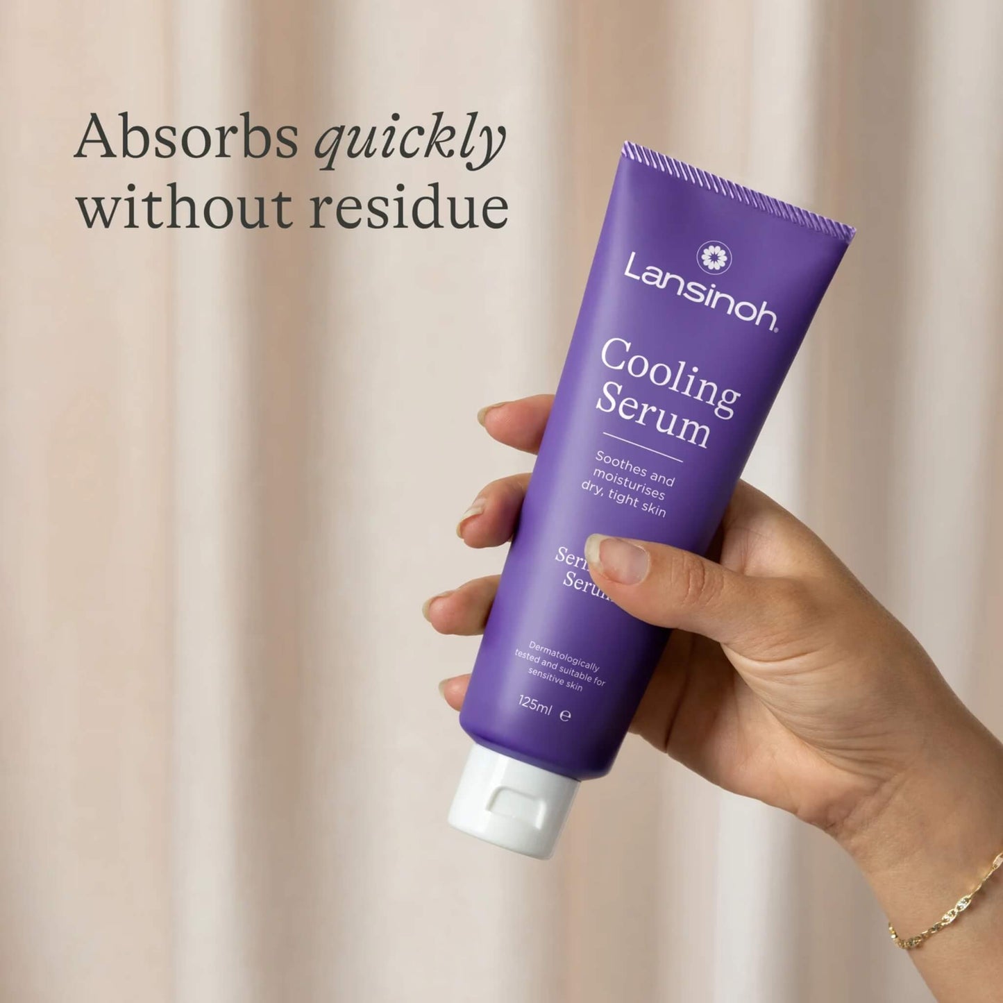 A hand holds a purple tube of cooling serum upright against a neutral curtain background.
