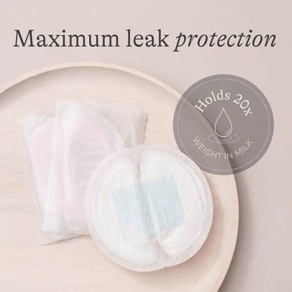 Close-up of disposable breast pads on a wooden surface showing their thin, contoured design and single-use wrappers.