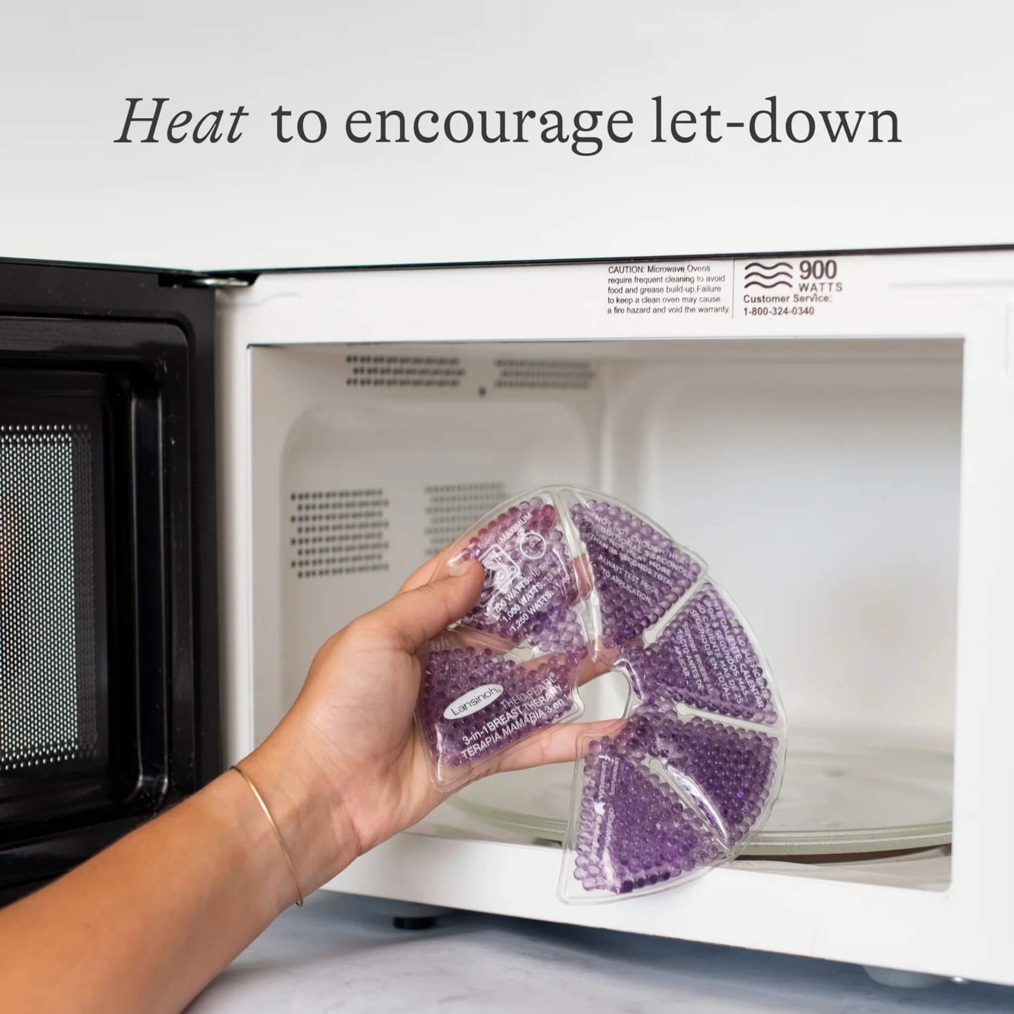 A hand placing a purple reusable breast therapy pack into a microwave to warm it before breastfeeding or expressing.