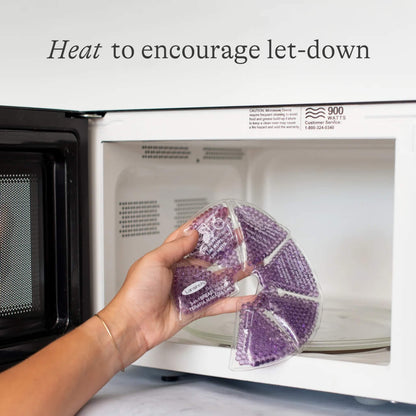 A hand placing a purple reusable breast therapy pack into a microwave to warm it before breastfeeding or expressing.