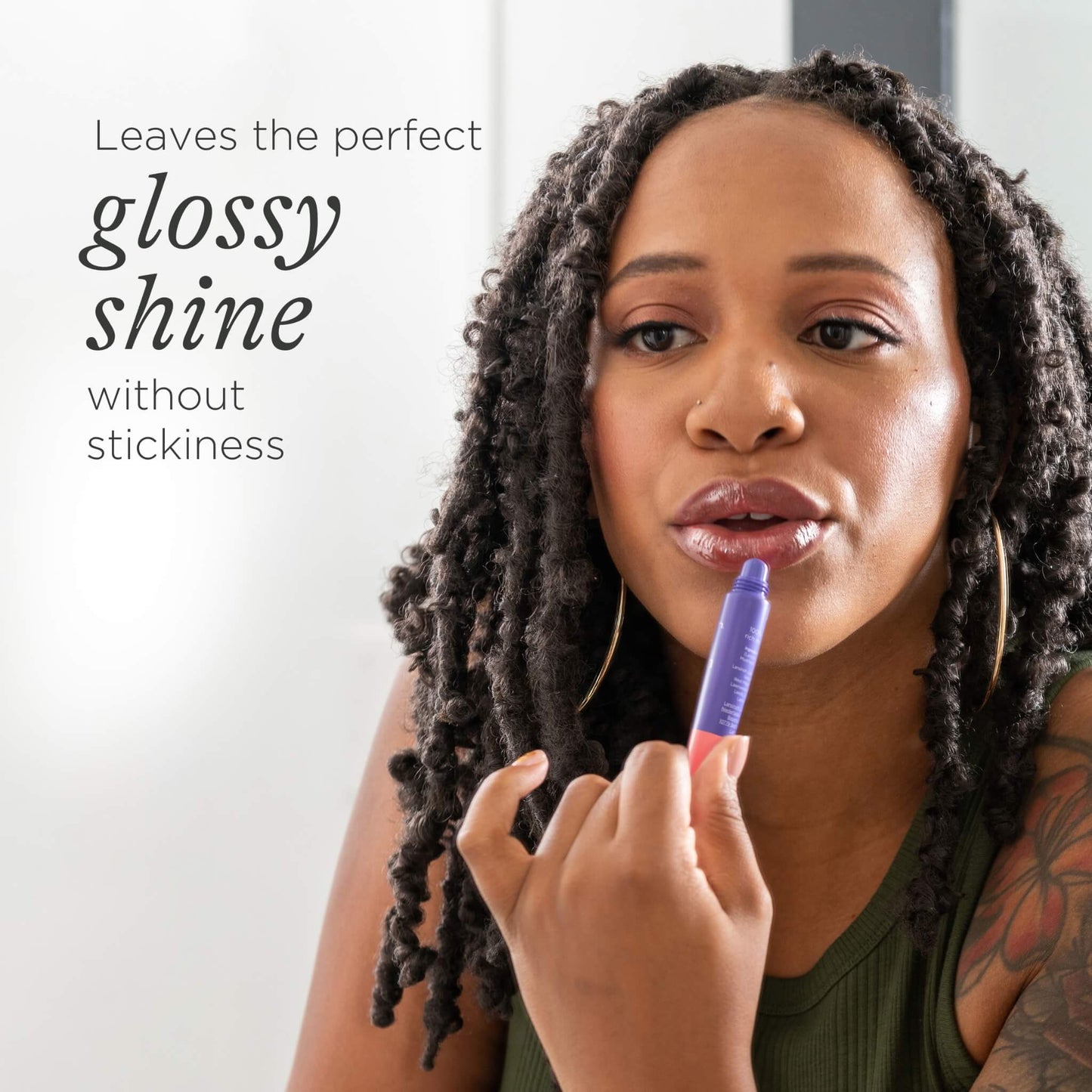 A woman applying lip balm to glossy lips while looking into a mirror.