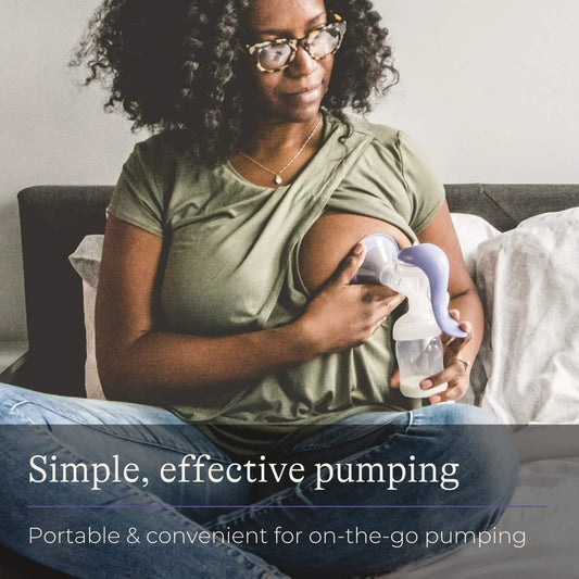 Mother sitting cross-legged on a bed using a manual breast pump to express milk, showing discreet and portable on-the-go use.