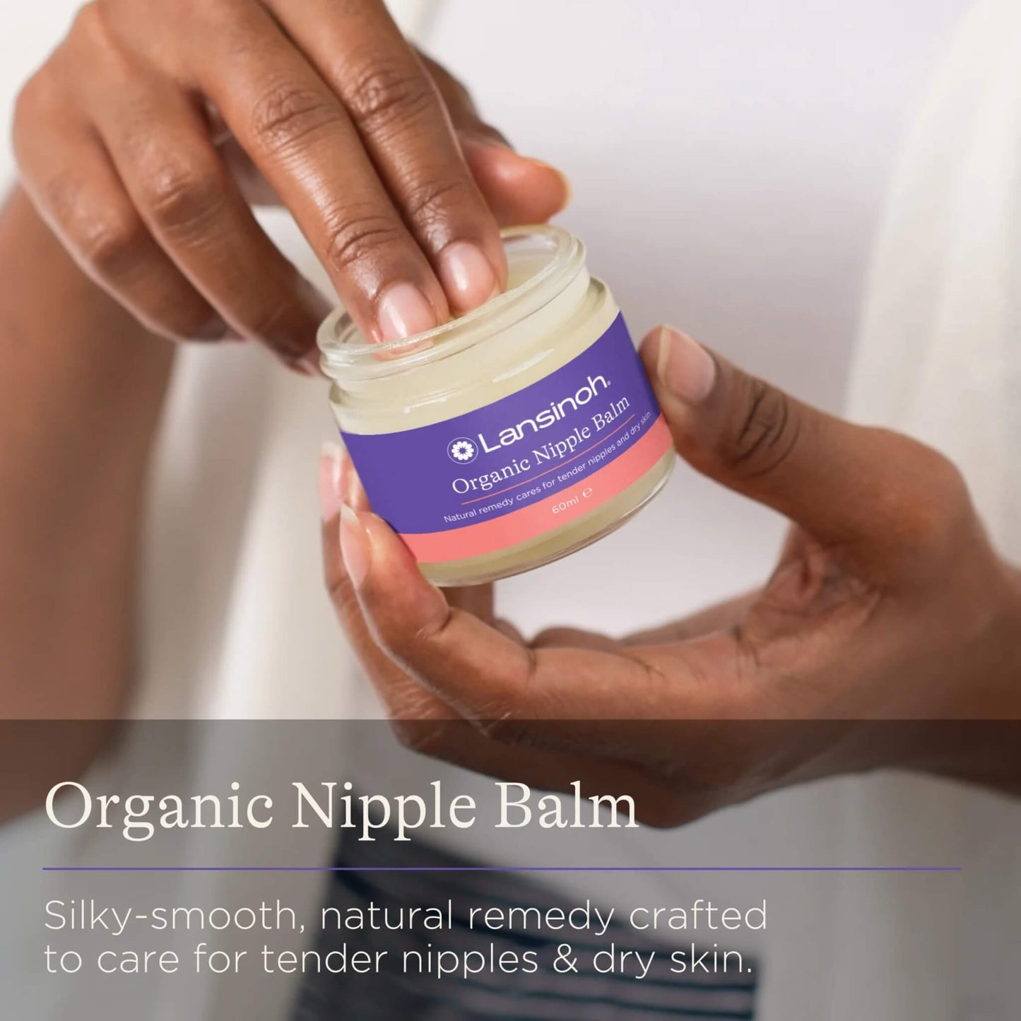 A woman dipping her finger into an open jar of nipple balm while holding the container in both hands.
