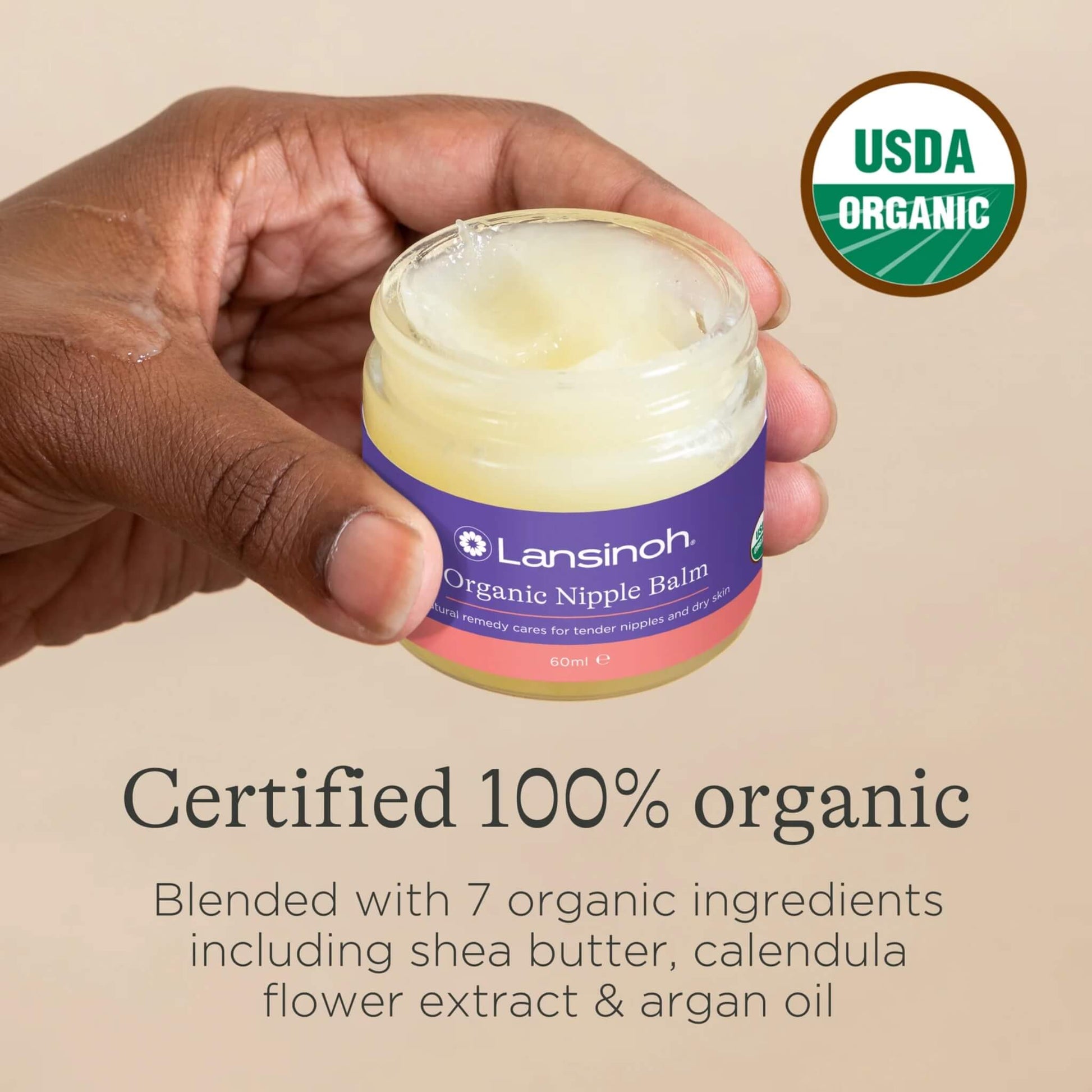 A hand holding an open jar of organic nipple balm with USDA Organic certification badge and ingredient information shown alongside.