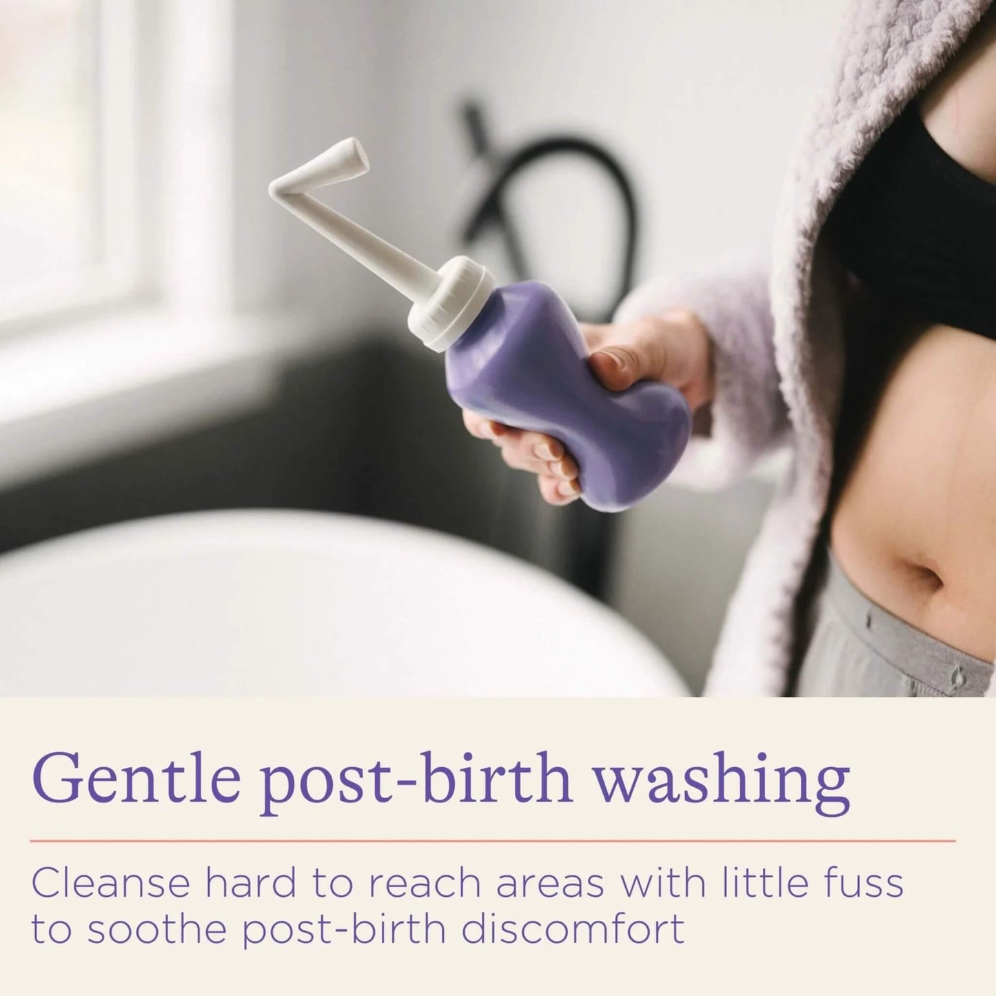 A woman holding a purple post-birth wash bottle beside a bath, showing the angled spout designed to help cleanse hard-to-reach areas after childbirth.