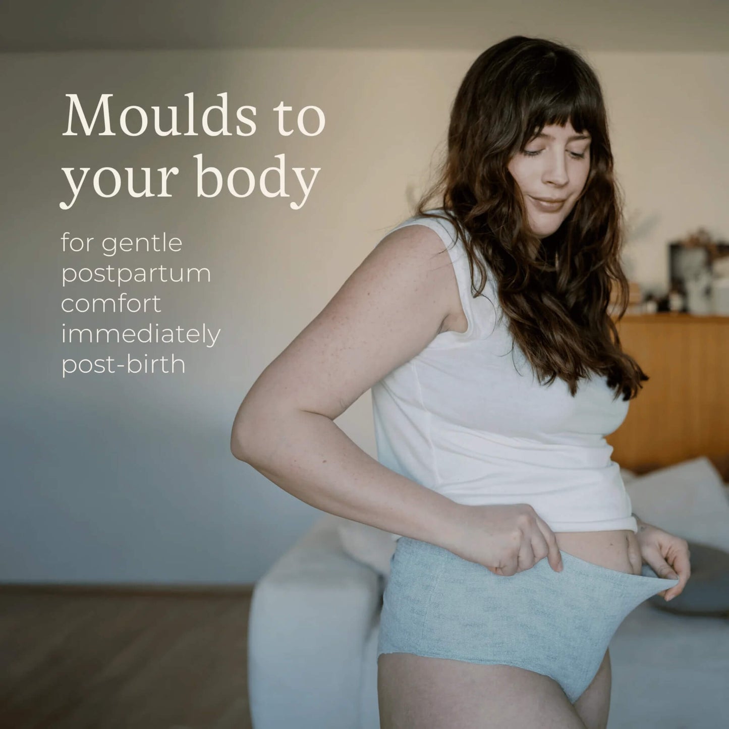A woman stretching a pair of grey postpartum underwear to demonstrate the flexible fabric that moulds comfortably to changing postpartum body shapes.