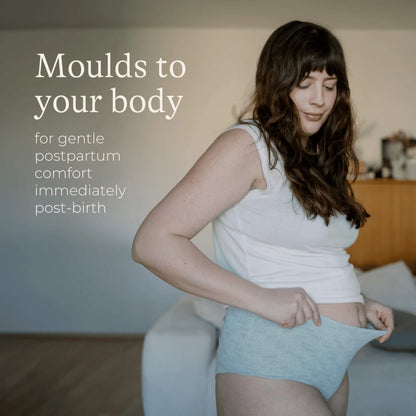 A woman stretching a pair of grey postpartum underwear to demonstrate the flexible fabric that moulds comfortably to changing postpartum body shapes.