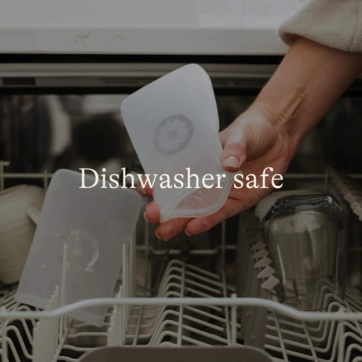Hand placing a silicone breastmilk storage bag into a dishwasher rack beside feeding accessories to show cleaning after use.