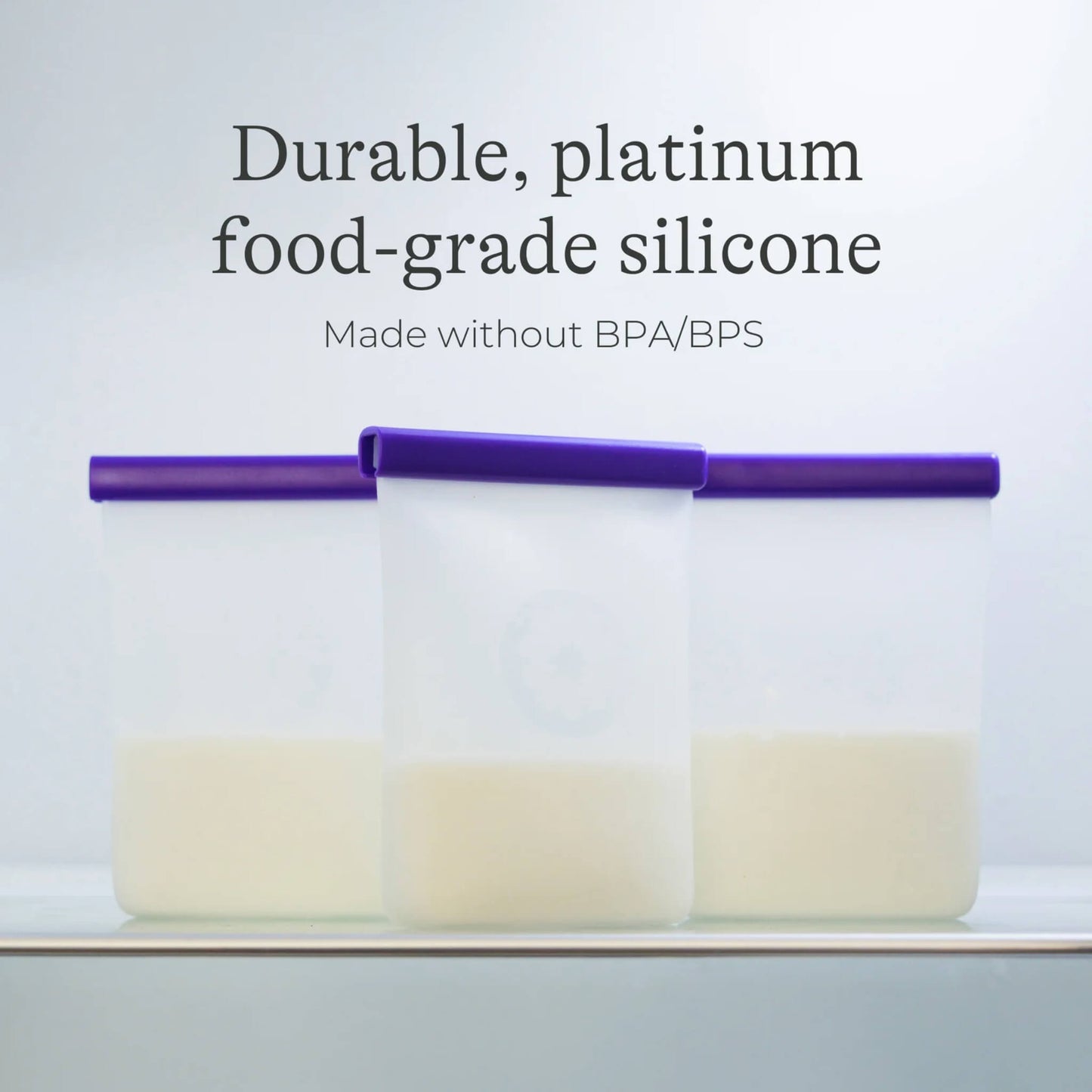 Three silicone breastmilk storage bags filled with milk standing upright in storage with purple sealing bars visible.