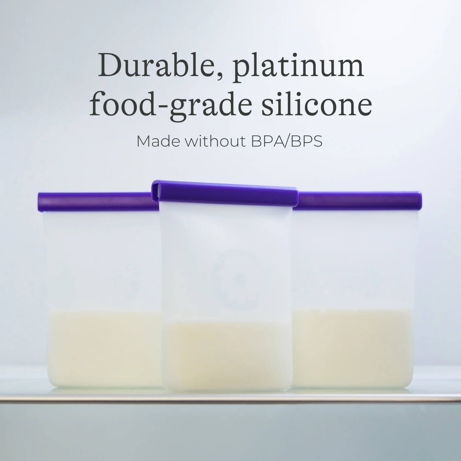 Three silicone breastmilk storage bags filled with milk standing upright in storage with purple sealing bars visible.