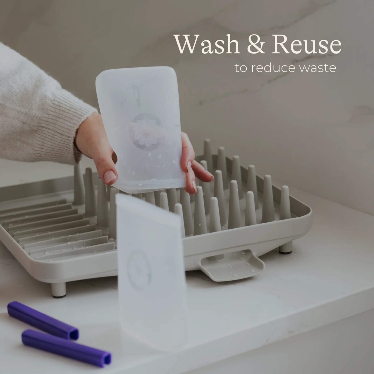 Hand holding and air drying reusable silicone breastmilk storage bags on a drying rack with sealing bars placed beside.