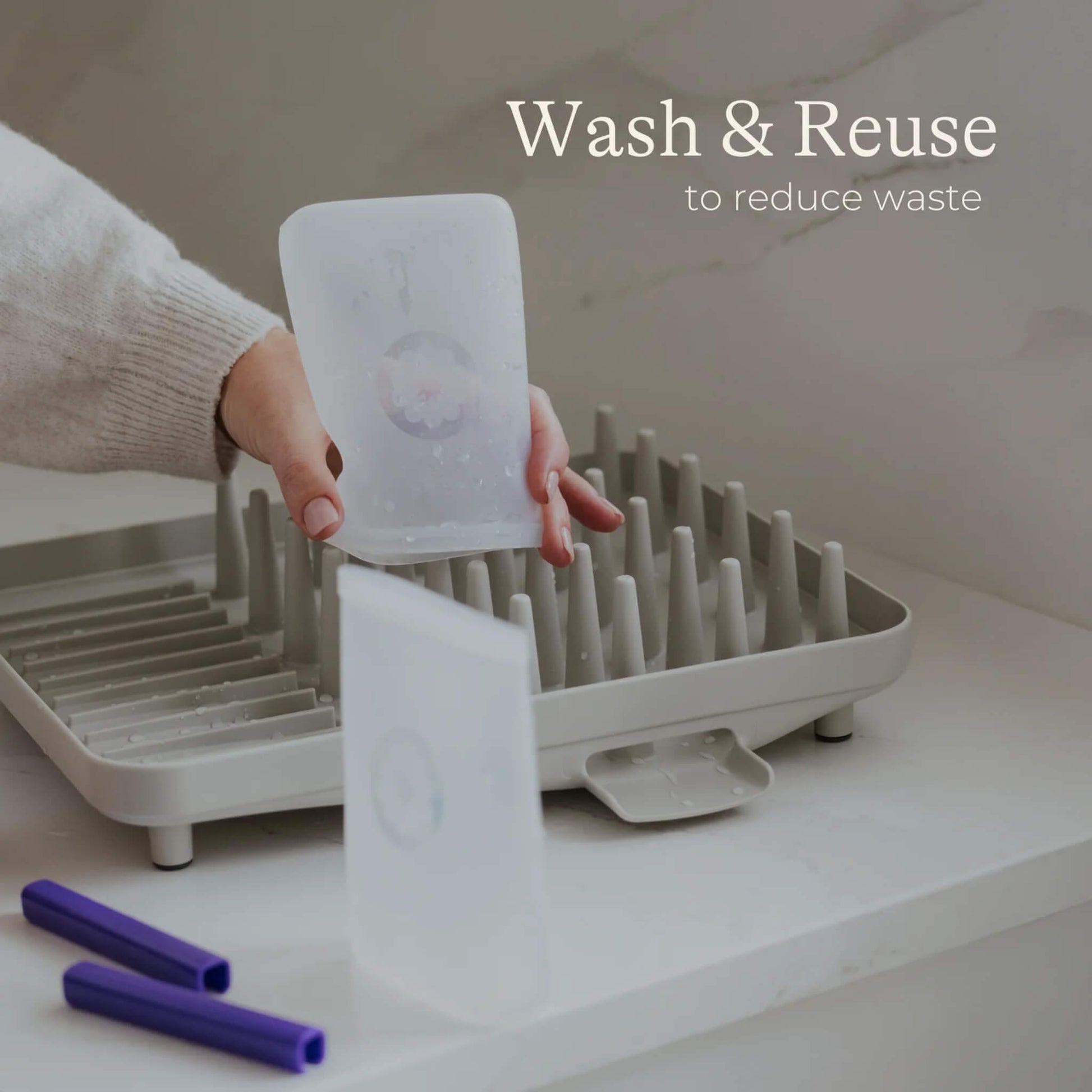 Hand holding and air drying reusable silicone breastmilk storage bags on a drying rack with sealing bars placed beside.