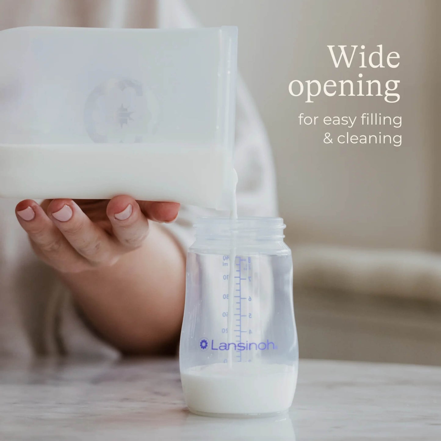 Breastmilk being poured from a wide-opening silicone storage bag into a baby bottle during milk transfer.