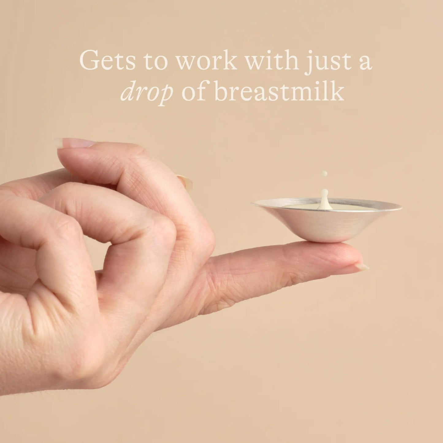 Close-up of hand balancing a silver nipple cup on one finger with a drop of breast milk inside, illustrating how only a small amount of milk is needed for soothing use.