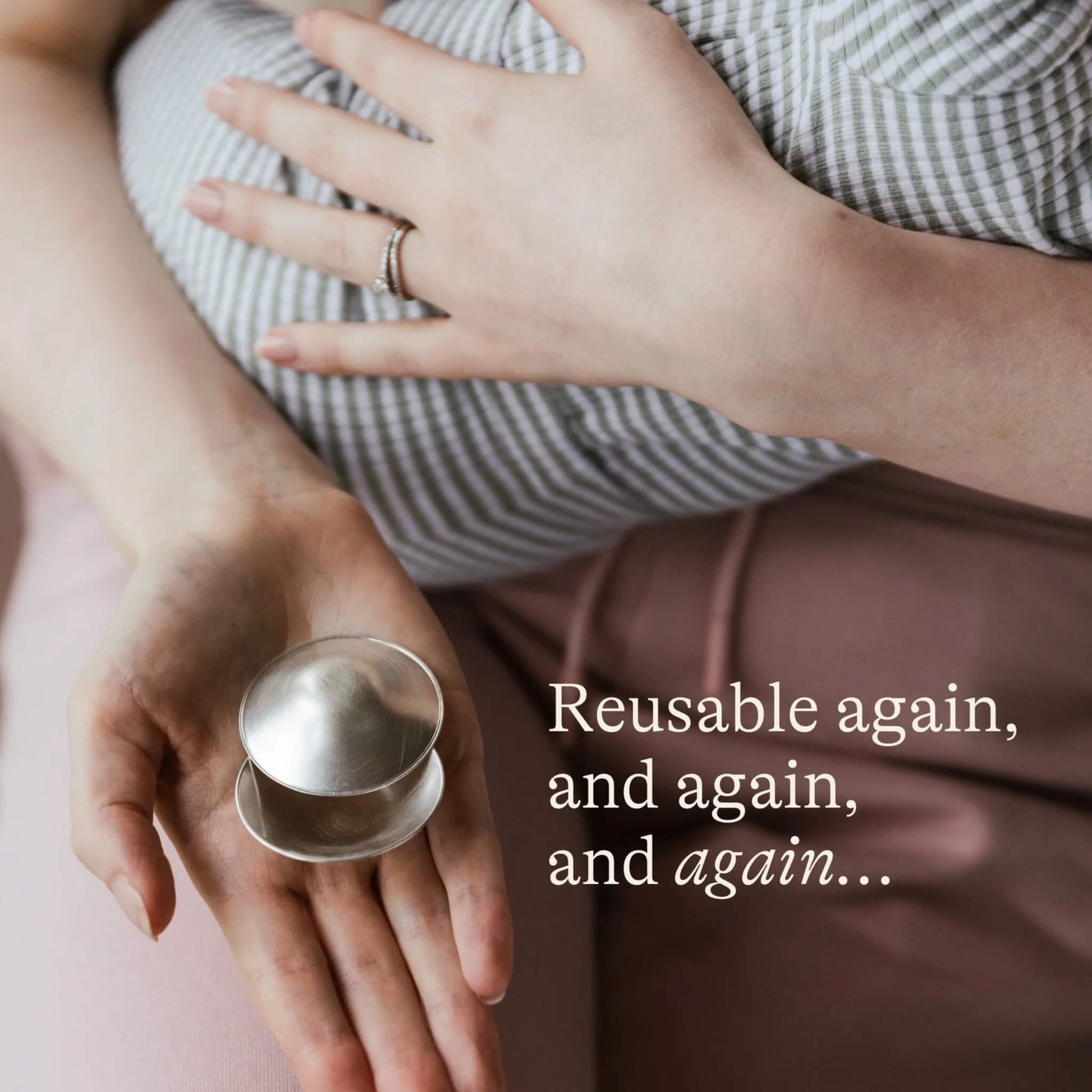 Mother resting a pair of silver nipple cups in her hand while cradling her baby, showing the reusable and durable nature of the Silverette design.