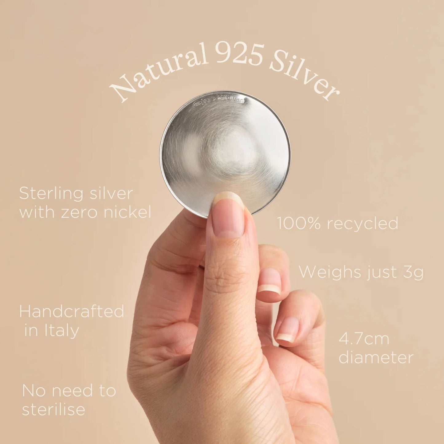 Hand holding a sterling silver nipple cup against a neutral background with text describing features such as 100% recycled 925 silver, handcrafted in Italy, and no need to sterilise.