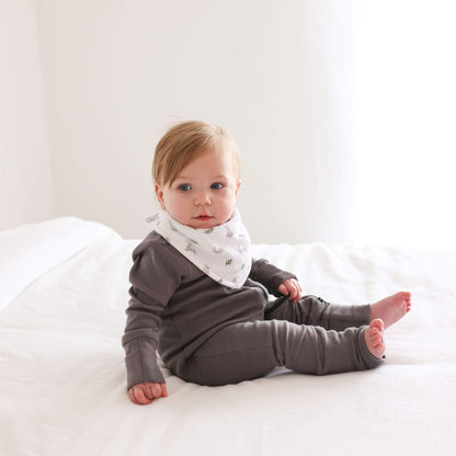Close-up of baby wearing white Lulujo bandana bib with bunny and fern pattern, displaying the soft fabric against delicate skin and stylish grey outfit coordination.