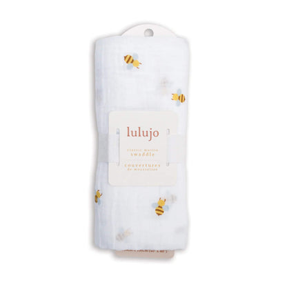 Muslin swaddle rolled in its Lulujo packaging with label visible, showing the bee print through the transparent layers.