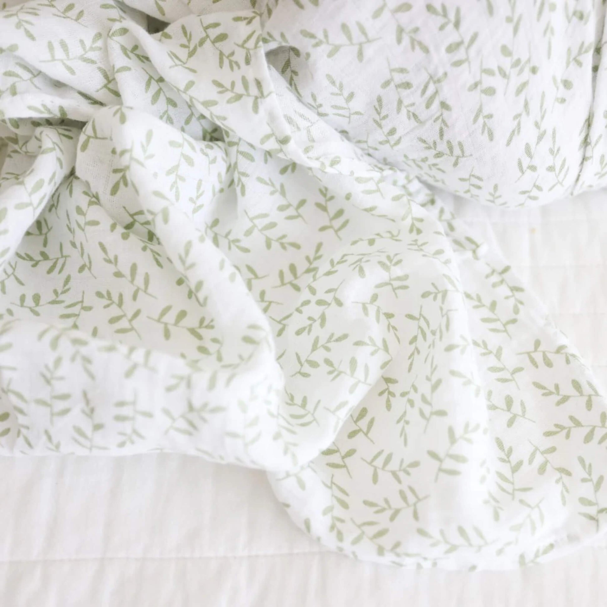 Close-up of the muslin fabric showing the gentle weave and scattered green leaf print.