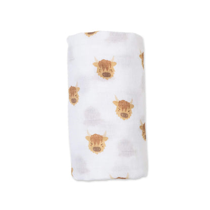 Lulujo Cotton Muslin Swaddle in the Highland Cow design, neatly rolled to show its soft white fabric decorated with playful brown Highland cow faces.