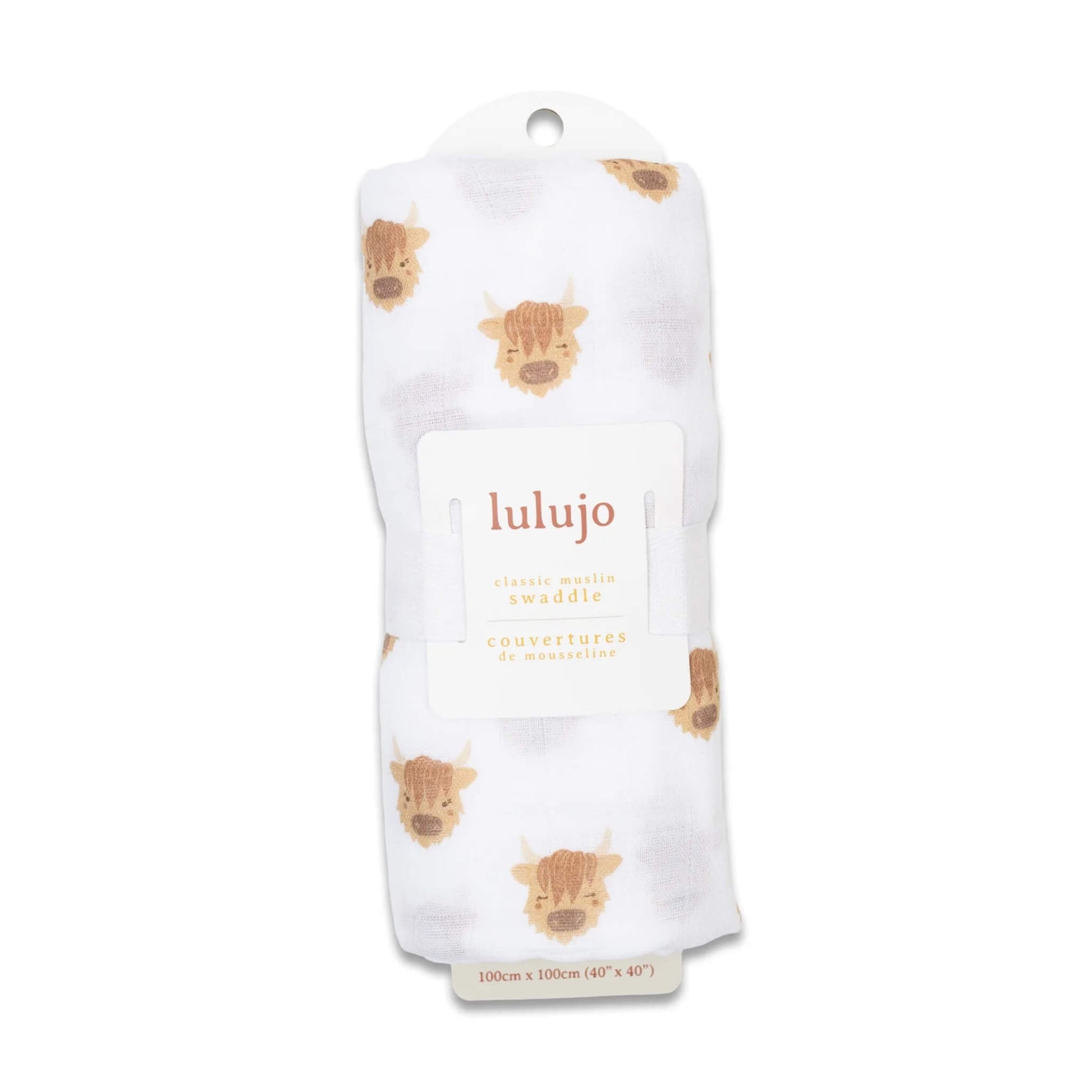 Swaddle rolled in its Lulujo packaging with the label visible, showing the cow motif through the white muslin fabric.