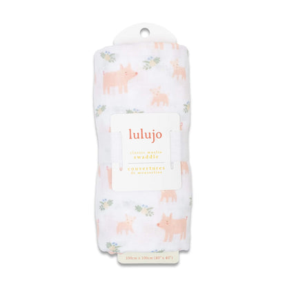Swaddle rolled in its Lulujo packaging with the label visible, showing the pale pink pig pattern through the fabric.