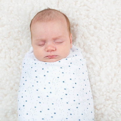Baby peacefully sleeping, wrapped in the white muslin blanket covered with tiny blue stars on a soft textured surface.