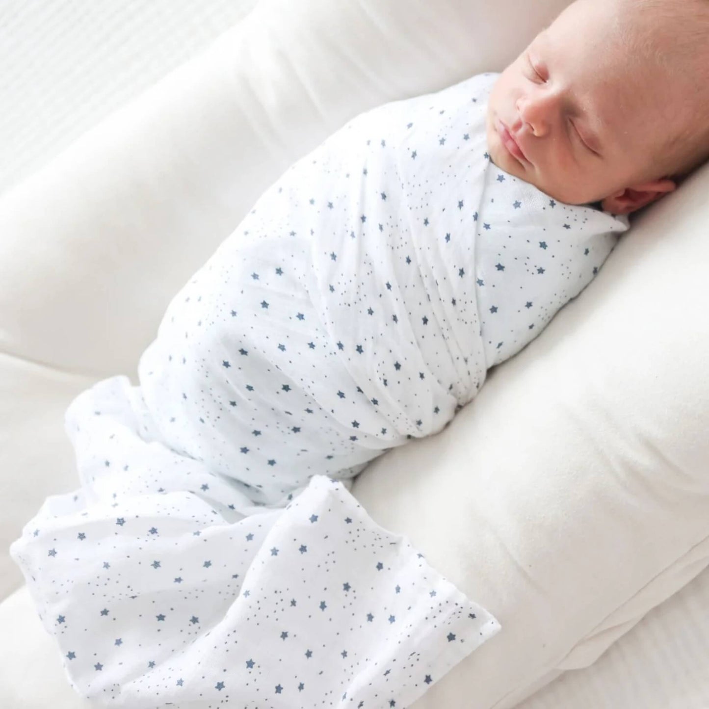 Close-up of the baby resting in the muslin swaddle with blue star print, showing the soft and breathable cotton texture.