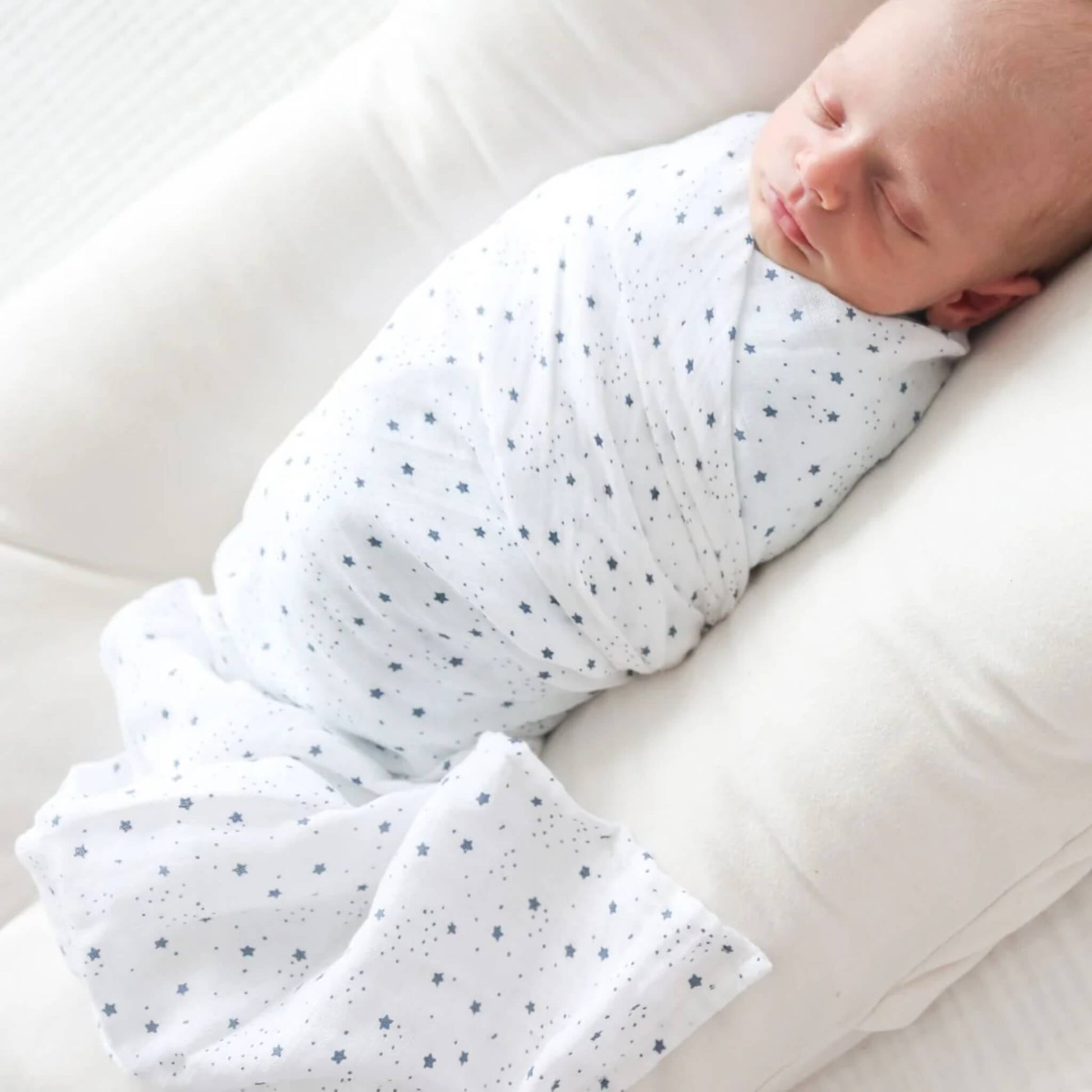 Close-up of the baby resting in the muslin swaddle with blue star print, showing the soft and breathable cotton texture.