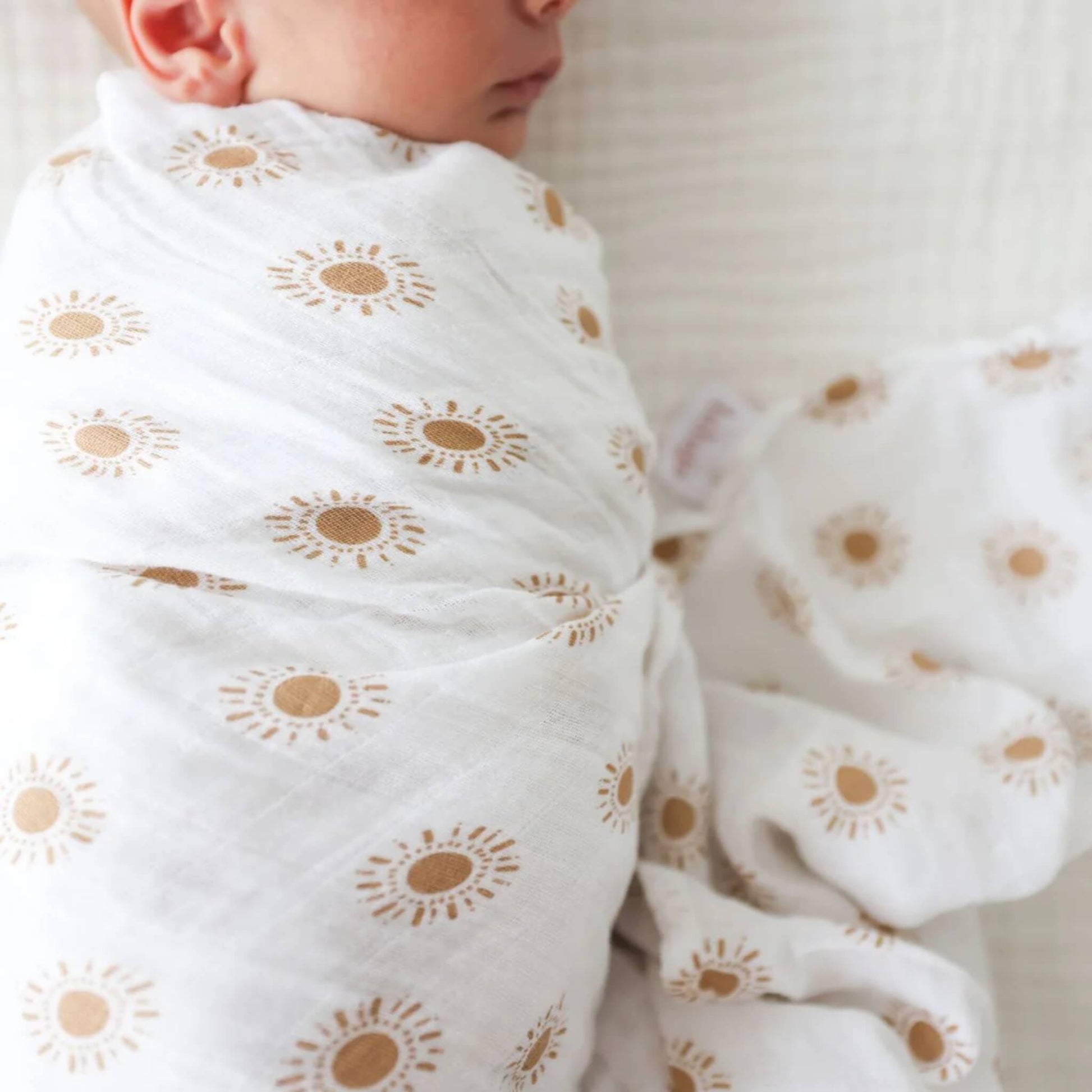 Close-up of cotton muslin fabric showing fine texture and golden sun design around a sleeping baby.