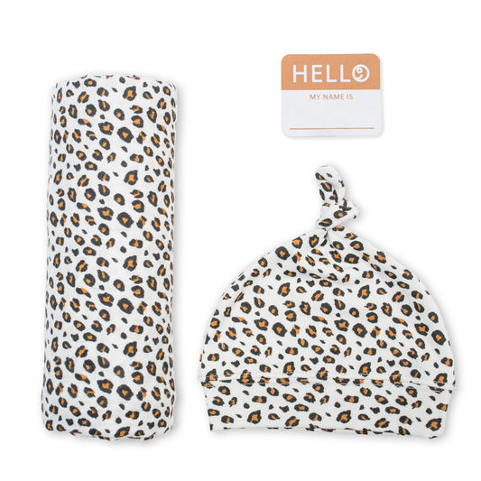 Lulujo Leopard Hello World Set featuring soft muslin swaddle blanket, matching knotted hat and orange name tag for stylish newborn photos.
