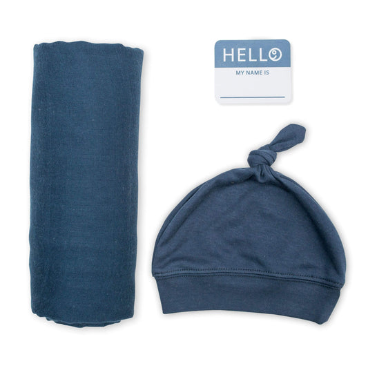 Lulujo Hello World set featuring soft navy blue muslin swaddle blanket, matching knotted beanie hat and personalized name tag for stylish newborn photos.