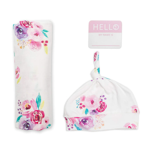 Lulujo Hello World newborn set featuring white muslin swaddle with watercolour floral print, matching top-knot hat and pink name tag sticker."