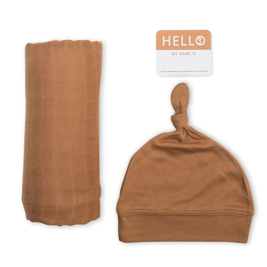 Lulujo Hello World set featuring soft caramel tan muslin swaddle, matching knotted hat and personalised name tag for gender-neutral newborn photos.