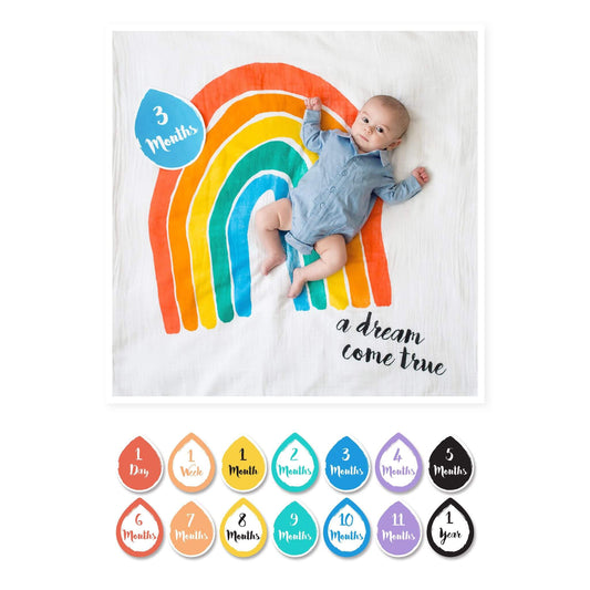  Lulujo Milestone Muslin Blanket "A Dream Come True" featuring 3-month-old baby in blue outfit positioned on vibrant rainbow design with coordinating milestone card.