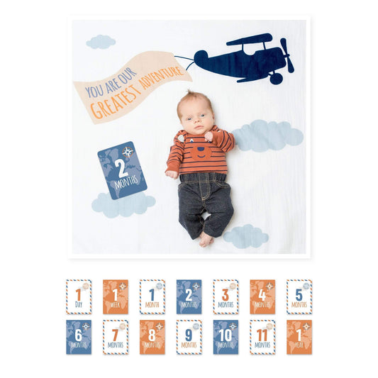 Baby at 2 months lying on Lulujo milestone blanket with blue airplane design and 'You Are Our Greatest Adventure' message alongside milestone cards."