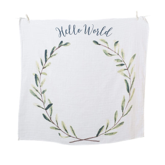 Lulujo white muslin blanket with 'Hello World' text and botanical wreath design hanging on clothesline, perfect for monthly baby photos.