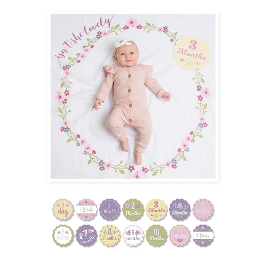 Lulujo Milestone Muslin Blanket "Isn't She Lovely" featuring a 3-month-old baby girl in pink ribbed outfit with floral wreath design and age marker card.