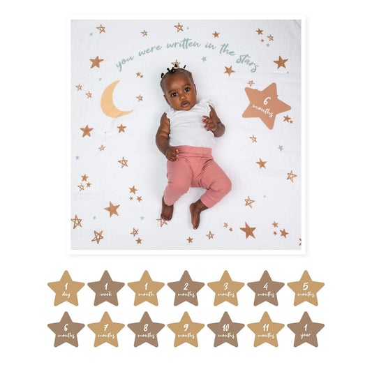 Six-month-old baby with white top and pink trousers on Lulujo 'Written in the Stars' milestone blanket featuring gold stars and crescent moon design, with star-shaped milestone cards.